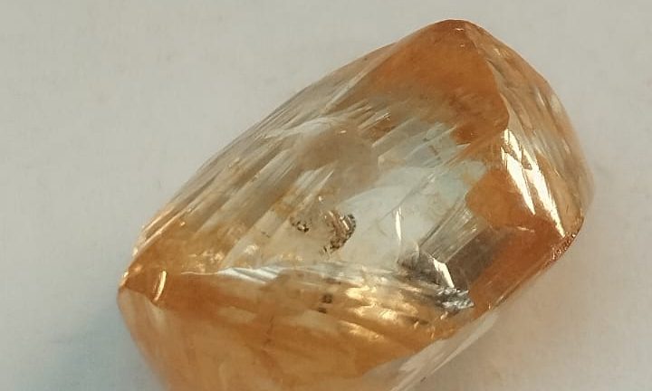 A faceted, elongated diamond crystal with a warm golden‑orange tint and reflective surfaces.