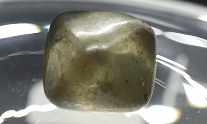 A small, rounded diamond crystal with a dull, cloudy coating covering its surface.