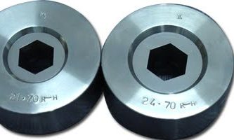 Two metallic wire‑drawing dies with hexagonal openings in the center, placed side by side. Each die has engraved markings along the outer surface.